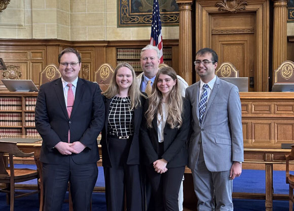 Law students smiling in front of a wooden filled court room