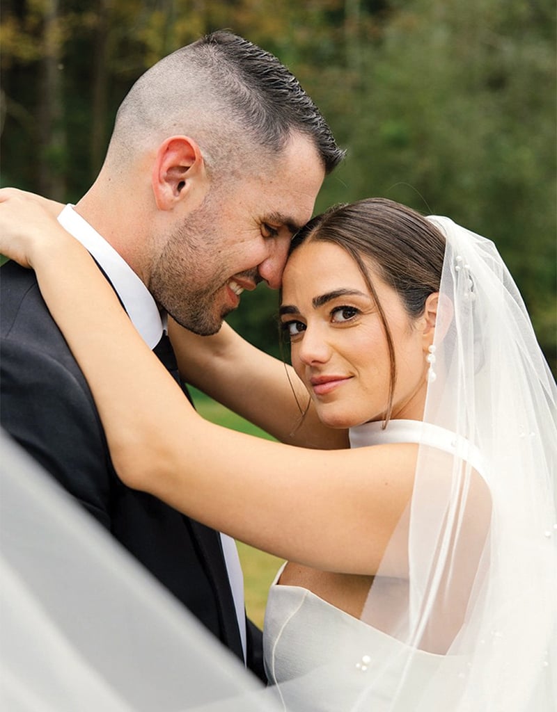 Savannah Reilly looks at the camera as her husband embraces her on their wedding day