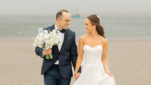 Laura Savage and Andrew Czuchra walk along the beach holding hands on their wedding day