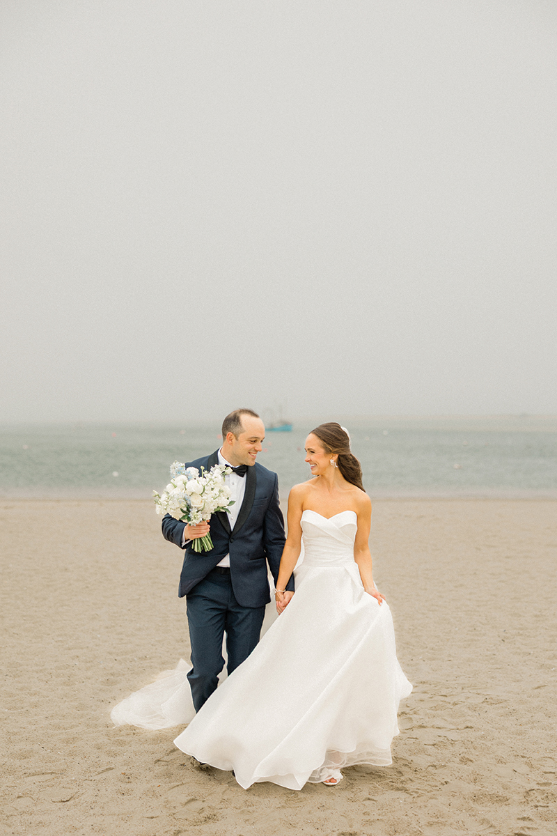 Laura Savage and Andrew Czuchra walk along the beach holding hands on their wedding day